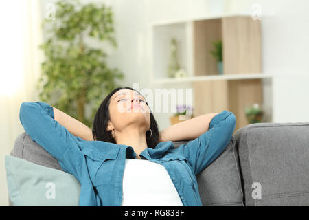 Relaxed woman resting with arms on head sitting on a sofa at home Stock Photo