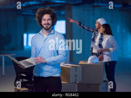 young male architect on construction site checking documents and business workflow using laptop computer with colleagues in the background in new star Stock Photo