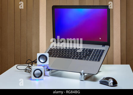 Small white speakers are connected with a USB cable to a running laptop. Stock Photo
