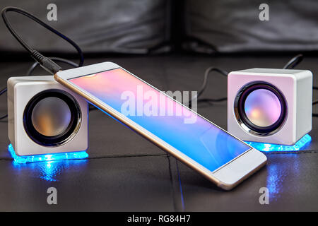 On the sofa seat there are two speakers with blue LEDs, which are connected to smartphone with cable. Stock Photo