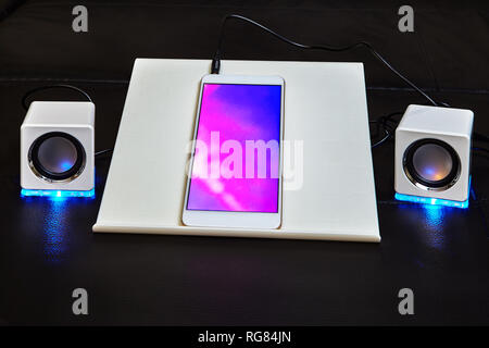 The smartphone is connected to two white cube-shaped speakers made of plastic and equipped with a blue led light. Stock Photo