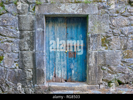 Rustic old blue wooden door, locked, showing aging and wear and tear on old stone building Stock Photo