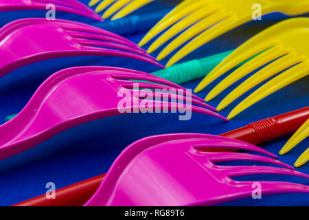 Yellow and pink cutlery plastic forks and straws arranged on blue background. Color trends and plastic waste problem concept Stock Photo