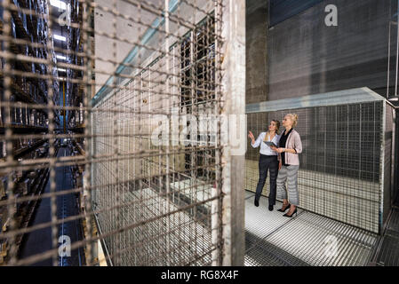 Women using laptop in high rack warehouse Stock Photo