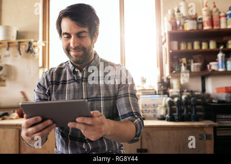 Smiling woodworker using a digital tablet in his workshop Stock Photo