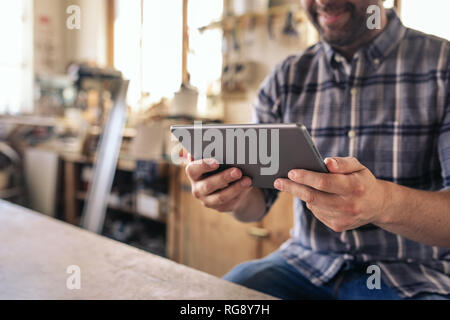 Woodworker sitting in his workshop using a digital tablet Stock Photo