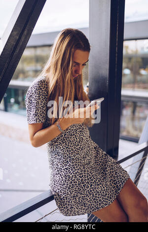 Attractive young woman in leopard print dress checking cell phone Stock Photo