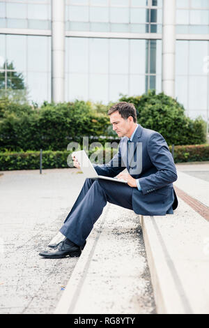 Serious businessman sitting down using laptop in the city Stock Photo