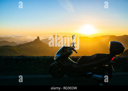 Spain, Canary Islands, Gran Canaria, parked motor scooter in front of mountainscape at sunset Stock Photo