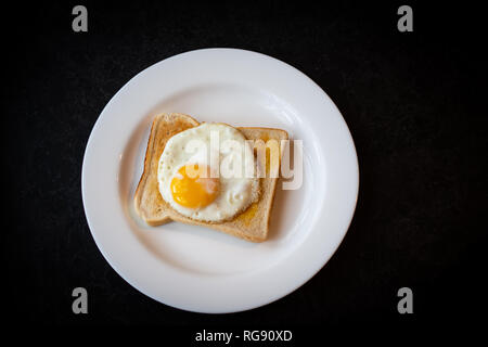 A perfect round sunny side up egg sits a top a slightly browned toast after being fried ready for breakfast. Stock Photo