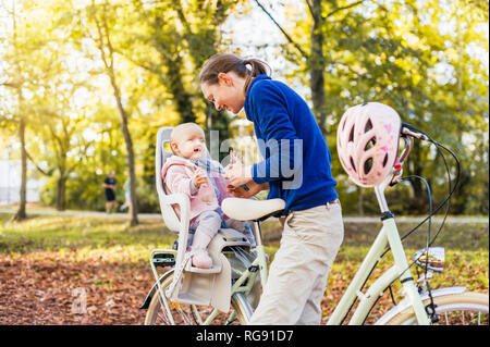 Mother and daughter riding bicycle, baby wearing helmet sitting in children's seat Stock Photo
