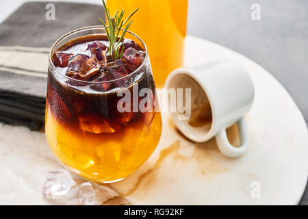 Orange juice espresso with ice, bottle of organic orange juice and empty espresso shot on white marble serving plate. Ice cold summer drink. Close up. Stock Photo