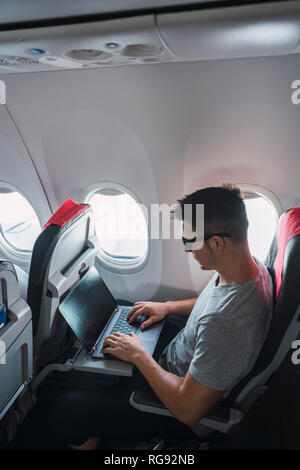 Man using laptop in airplane Stock Photo