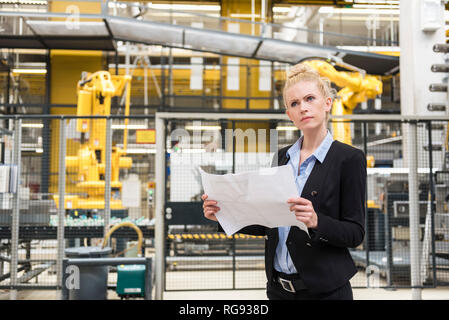 Woman holding plan in factory shop floor with industrial robot Stock Photo