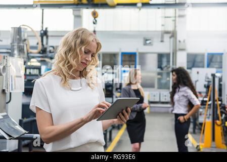 Woman using tablet in factory shop floor with two women in background Stock Photo