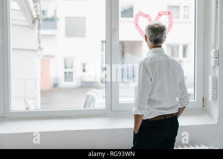 Businessman looking out of a window with a heart-shape on it, rear view Stock Photo
