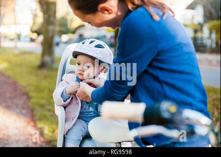 Mother and daughter riding bicycle, baby wearing helmet sitting in children's seat Stock Photo