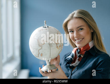 Portrait of smiling young stewardess with globe Stock Photo