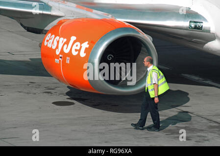 Close up of aircraft wing & jet engine nacelle pod on easyjet passenger airplane on tarmac at Stansted Airport with ground crew in high vis jacket UK Stock Photo