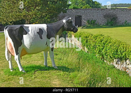 Friesian cow plastic model placed in grass field beside Ha Ha trench ditch with retaining wall to protect garden from cattle entering England UK Stock Photo