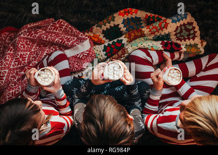 Three children sitting on a couch drinking hot chocolate Stock Photo