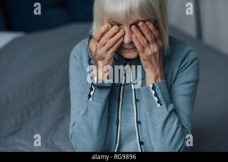 upset senior woman with glasses and grey hair wiping tears and crying at home Stock Photo