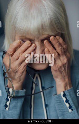 portrait of senior woman with glasses and grey hair wiping tears and crying at home Stock Photo