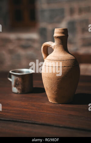 An old clay jug and with a glass stand on the wooden table. Stock Photo