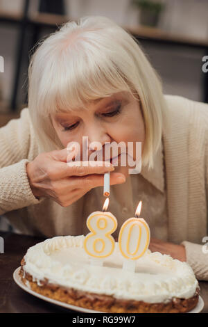 senior woman lighting up cigarette from burning candles on birthday cake at home Stock Photo