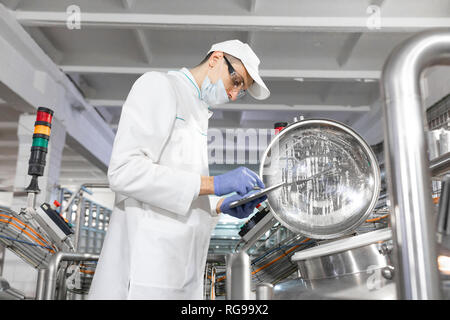 man in a white robe and a mask with a tablet in his hands is near can in the shop Stock Photo