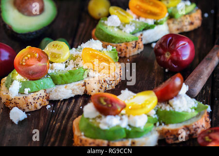 Avocado toast sandwich with avocadeos, fresh from the garden heirloom tomatoes and feta cheese, Greek food and healthy vegetarian diet concept, over a Stock Photo