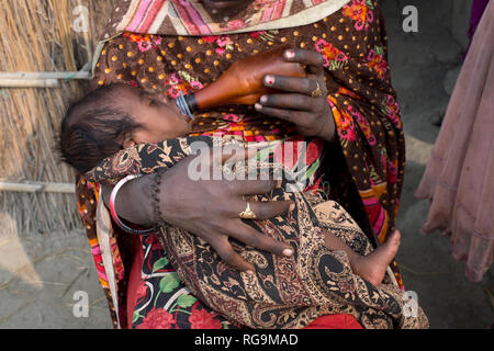 India. Bihar.  A 13 year old girl bottlefeeds her two month old brother.Their mother (who had 8 other children) died a month ago from TB. Stock Photo