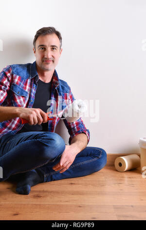 Man sitting on a parquet floor prepared with paint material to repaint his house. Front view. Vertical composition. Stock Photo