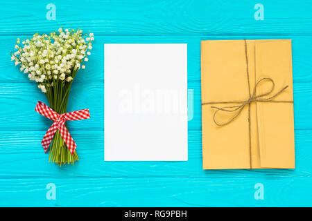 Craft envelopes, white blank note card and bouquet of lilies of the valley. mockup. Top view and flat lay with copy space. Stock Photo