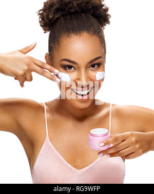 Laughing girl applying moisturizing cream on her face. Photo of beautiful african american girl with flawless skin on white background. Cosmetology Stock Photo