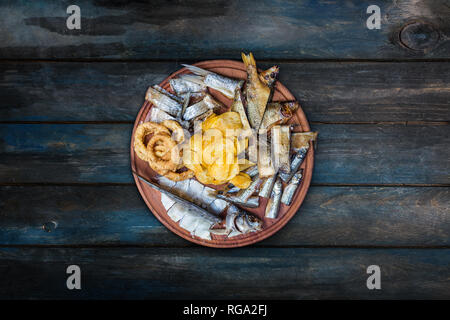 Beer snacks set. Salted, dried fish, squid rings and potato chips,served on the cutting board. Stock Photo