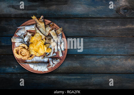 Beer snacks set. Salted, dried fish, squid rings and potato chips,served on the cutting board. Stock Photo