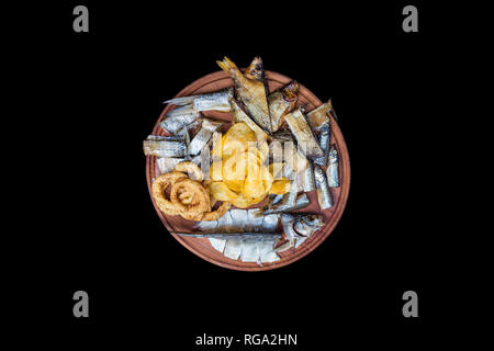 Beer snacks set. Salted, dried fish, squid rings and potato chips,served on the cutting board. Stock Photo