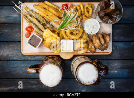 Beer snacks set. Fish set served on cutting board with the mugs, on the wooden background. Stock Photo