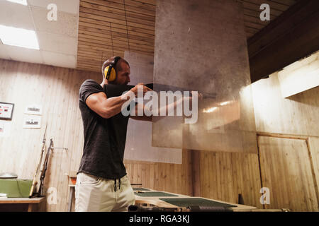 Man aiming with a rifle in an indoor shooting range Stock Photo