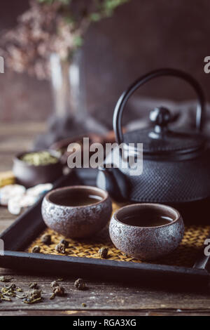 Still-life of japanese healthy green tea in a small cups and teapot over dark background Stock Photo