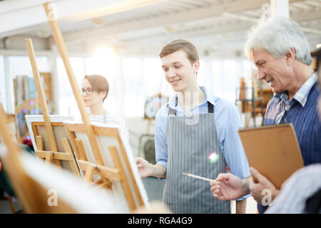 Waist up portrait of smiling teenage boy painting picture on easel in art studio, copy space Stock Photo