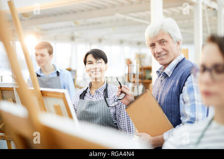 Portrait of mature art teacher smiling at camera posing with students in class, copy space Stock Photo