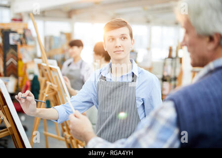 Waist up portrait of student in art class looking at teacher while painting picture on easel, copy space Stock Photo