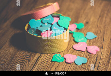 Gift pink box in the form of a heart filled with multi-colored small hearts on a wooden background. Stock Photo