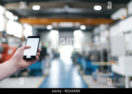 Hand holding laptop with blank screen in a factory workshop Stock Photo