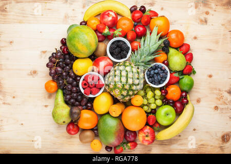 Circle filled with healthy colorful fruits, strawberries raspberries oranges plums apples kiwis grapes blueberries mango persimmon on light wooden tab Stock Photo