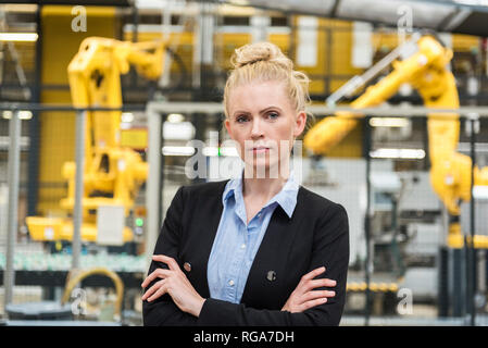 Portrait of confident woman in factory shop floor with industrial robot Stock Photo