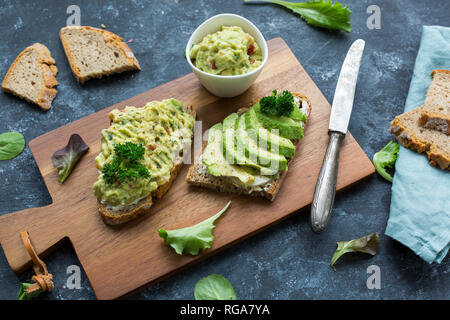 Slices of bread with sliced avocado and avocado cream on wooden board Stock Photo