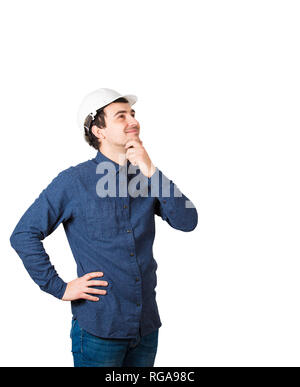 Cheerful positive thinking young man engineer wearing protective helmet holding hand under chin pensive looking up isolated over white background with Stock Photo